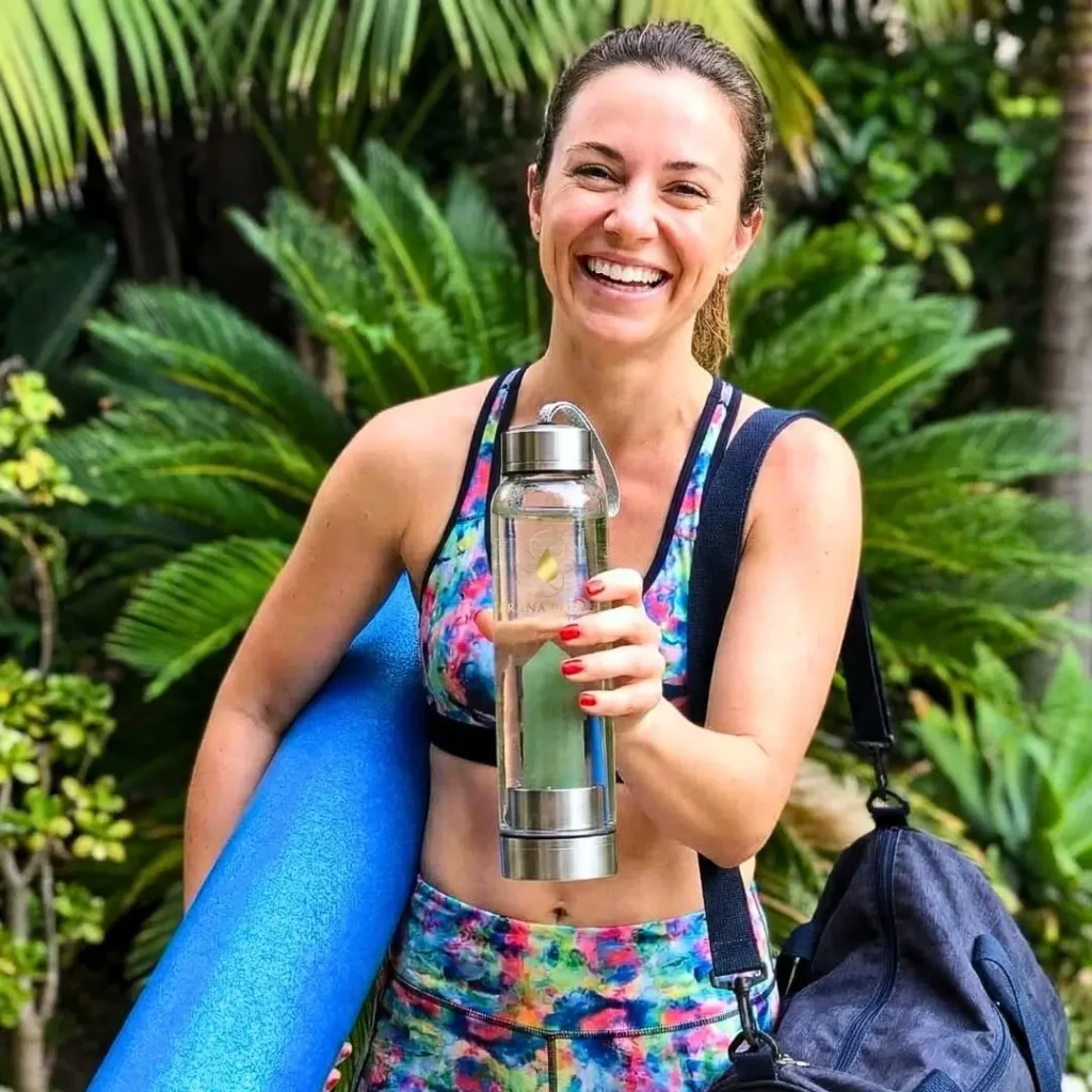 Boldog sportoló nő zöld aventurin kristálykulaccsal, polifoam hengerrel és sporttáskával trópusi háttérben - Prana Drops aktív életmód