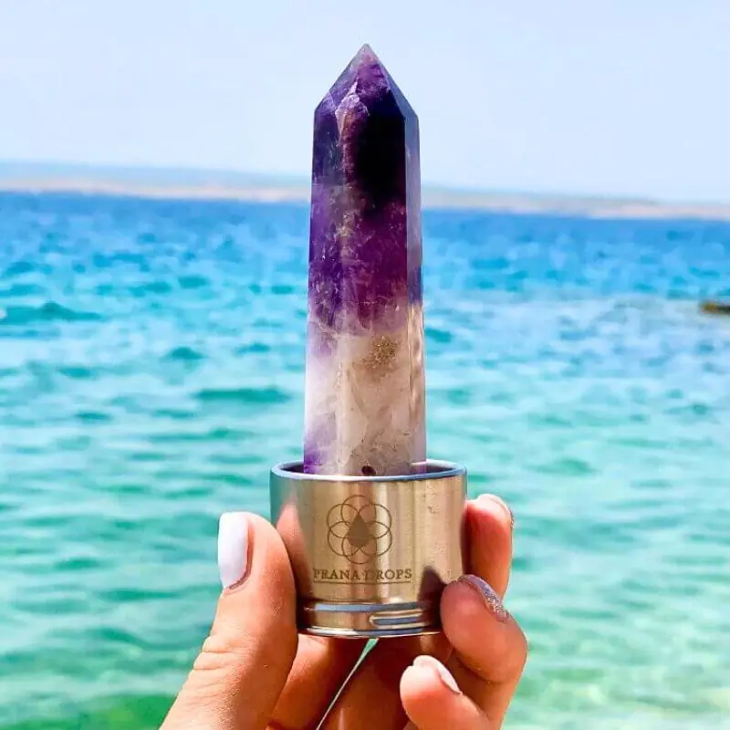 Cserélhető ametiszt kristálybetét kézben tartva tenger előtt