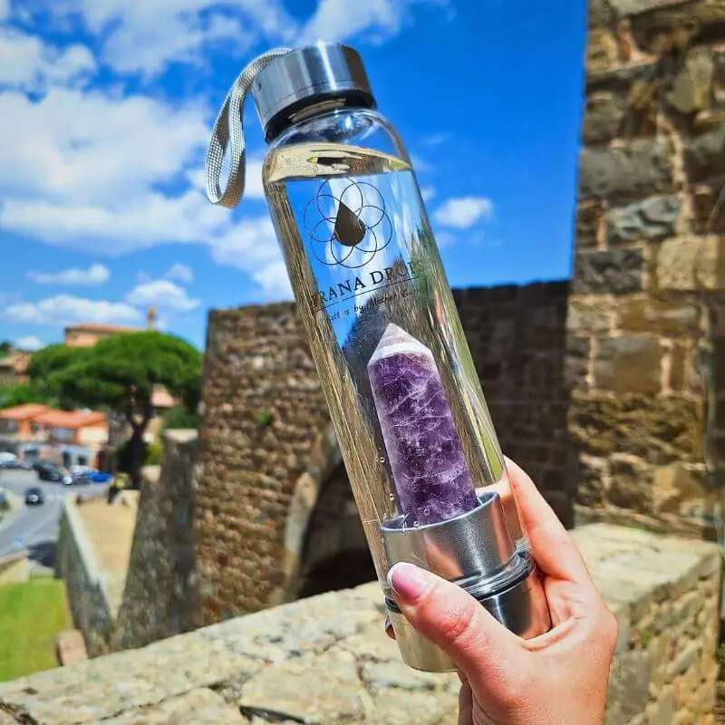Prana Drops ametiszt kristálykulacs kézben tartva történelmi városban - elegáns design